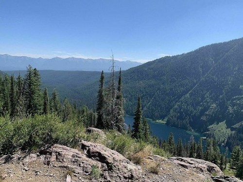 A scenic view of a lush green valley with a lake, surrounded by mountains under a clear blue sky.
