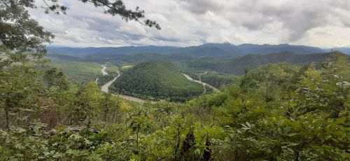 A panoramic view of rolling green hills and a winding river under a cloudy sky.