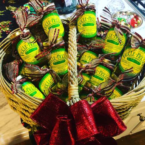 A festive basket filled with jars of pickles, each adorned with colorful ribbons and a shiny red bow.
