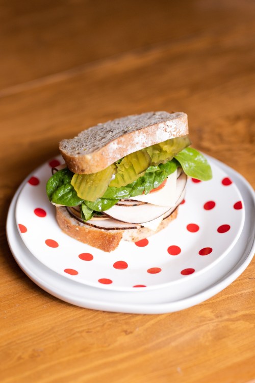 A sandwich with turkey, lettuce, and pickles on whole grain bread, served on a polka dot plate.