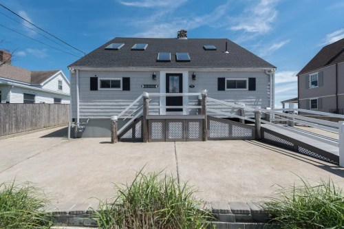 A gray house with a sloped roof, solar panels, and a ramp, set against a blue sky and grassy foreground.