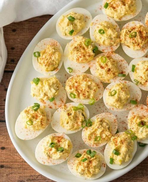 A platter of deviled eggs topped with paprika and green onions, arranged neatly on a white dish.