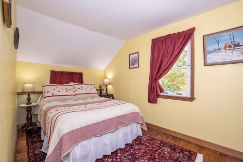 Cozy bedroom with a yellow wall, a double bed with a patterned blanket, and a window with red curtains.
