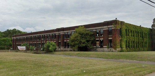 A large, brick building covered in ivy, set in a grassy area under a cloudy sky.