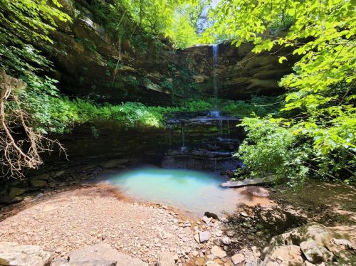 A serene waterfall cascades into a turquoise pool, surrounded by lush greenery and rocky terrain.