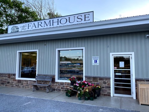 Exterior of a building labeled "the FARMHOUSE," featuring large windows and flower displays outside.
