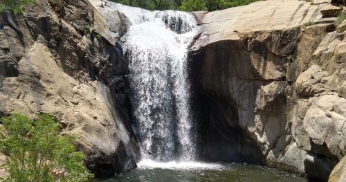 A serene waterfall cascading over rocky cliffs into a calm pool surrounded by greenery.