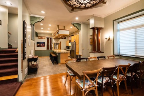A spacious dining area with a large table, leading to a modern kitchen and staircase in a well-lit home.