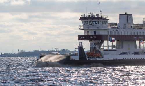 A ferry named Dewitt C. Greer navigates through shimmering water under a cloudy sky.