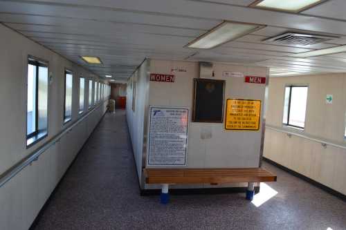 Interior corridor with signs for "Women" and "Men," featuring a plaque and informational board on the wall.