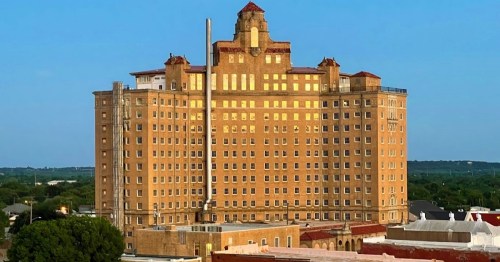 Historic hotel building with a distinctive tower, featuring a brick facade and red-tiled roof against a clear blue sky.