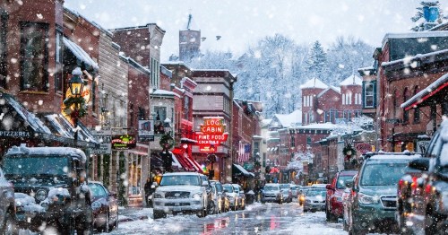 A snowy street scene with festive decorations, lined with shops and cars, creating a cozy winter atmosphere.