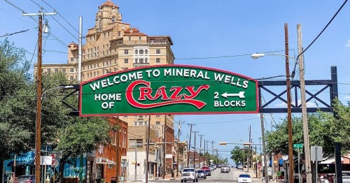 A green welcome sign for Mineral Wells, Texas, featuring "Home of Crazy" and indicating 2 blocks ahead.