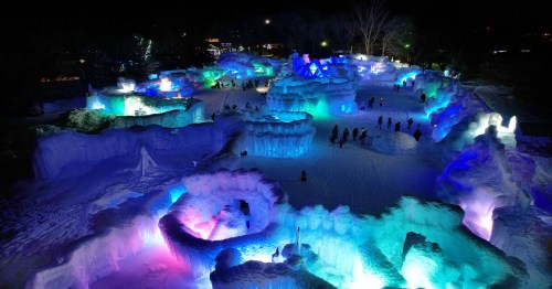 A colorful ice sculpture park illuminated at night, featuring intricate ice formations and visitors exploring the area.