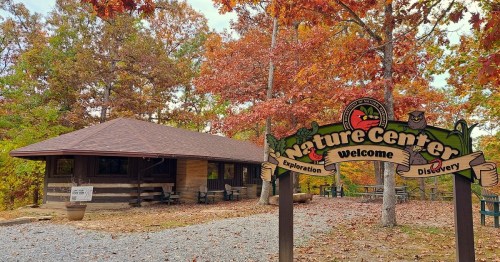 A rustic nature center surrounded by autumn foliage, featuring a welcoming sign and gravel pathway.
