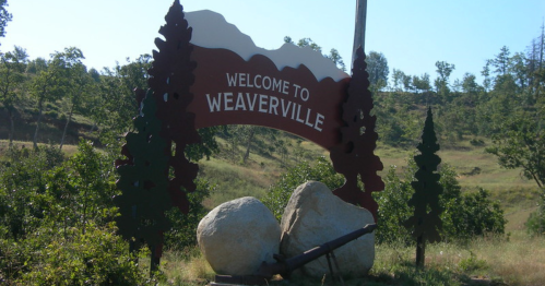 Sign welcoming visitors to Weaverville, framed by trees and mountains in the background.