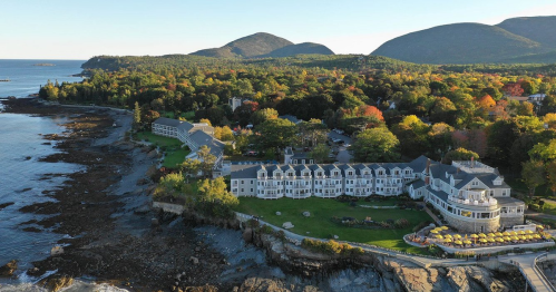 Aerial view of a coastal resort surrounded by autumn foliage and mountains, with rocky shoreline and calm waters.
