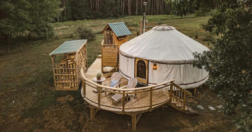 A cozy yurt with a wooden deck, surrounded by trees, featuring two chairs and a small shed nearby.