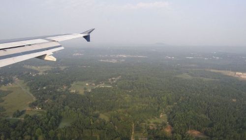 View from an airplane wing over lush green landscapes and distant hills during descent.