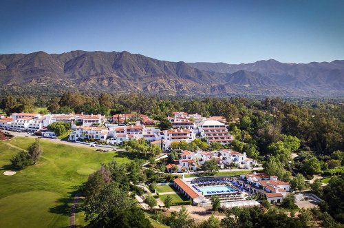 Aerial view of a resort with a pool, surrounded by lush greenery and mountains in the background.