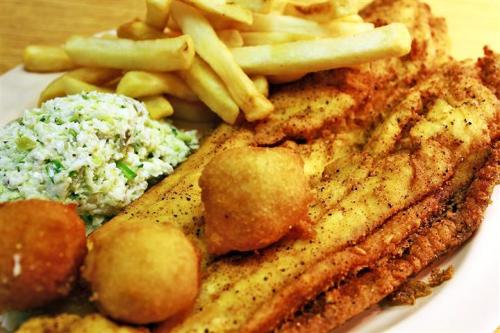 A plate of fried fish fillets, hushpuppies, coleslaw, and French fries.