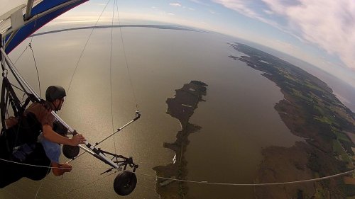 A person hang gliding over a vast body of water, with islands and green land visible in the distance.