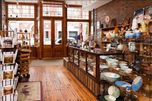 A cozy shop interior featuring wooden floors, display cases with pottery, and a welcoming entrance.