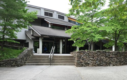 A modern building with a stone staircase, surrounded by green trees and landscaping.