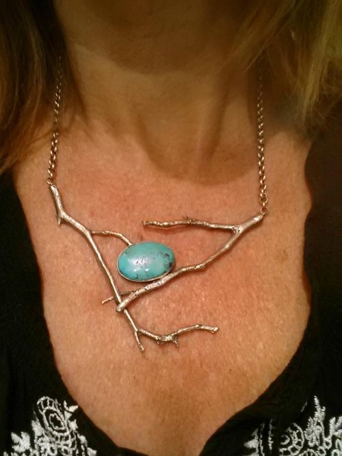 A unique necklace featuring silver branch-like design with a turquoise stone at the center, worn on a person's neck.