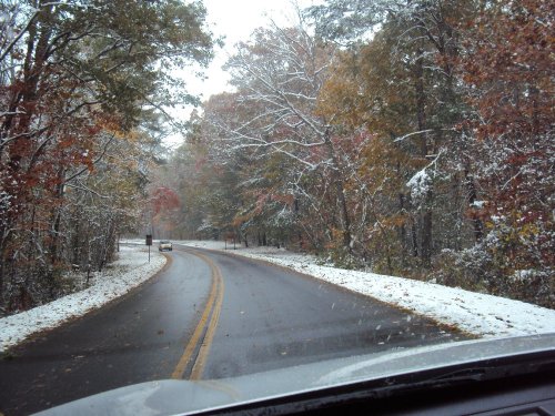 A winding road through a forest with autumn leaves and a light dusting of snow.