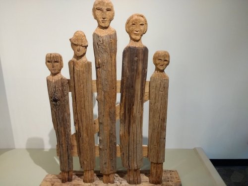 Wooden sculptures of five stylized figures with distinct facial features, standing together on a base.