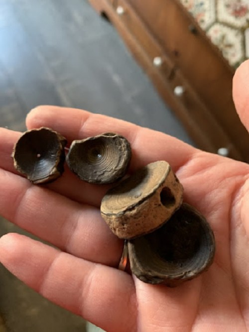A hand holding four small, round wooden pieces with hollow centers and varying textures.