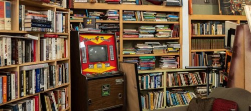 A cozy room filled with bookshelves stacked with books and a vintage arcade game in the corner.