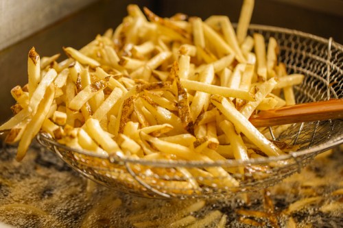 A metal strainer lifting golden-brown French fries from hot oil.