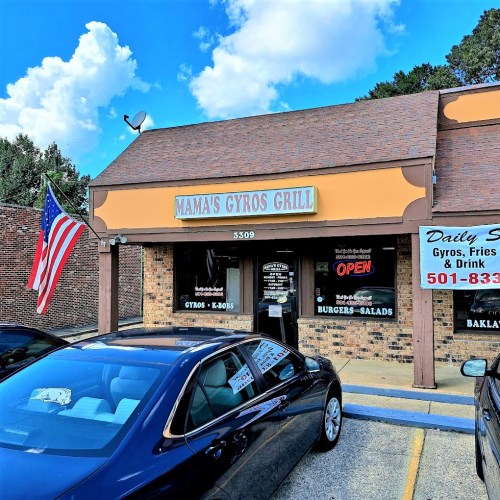 Exterior of Mama's Gyros Grill with an open sign, American flag, and parked car in front. Bright blue sky above.