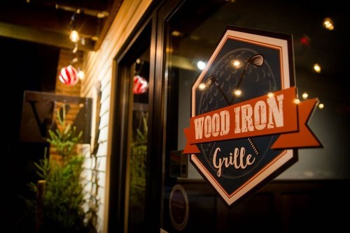 Sign for "Wood Iron Grille" on a restaurant door, illuminated by warm lights in a cozy outdoor setting.