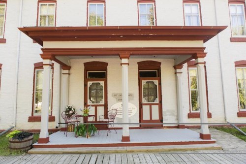 A charming porch with decorative columns, a small table, and chairs, set against a historic building with large windows.