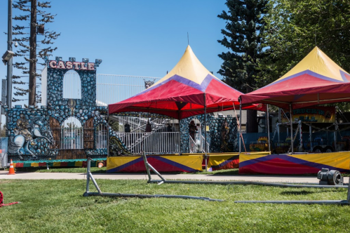 Colorful tents and a castle structure set up in a grassy area, with trees and a clear blue sky in the background.
