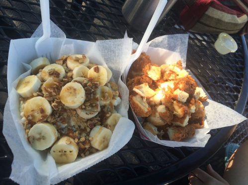 Two food trays on a table: one with sliced bananas, granola, and syrup; the other with fried chicken pieces.