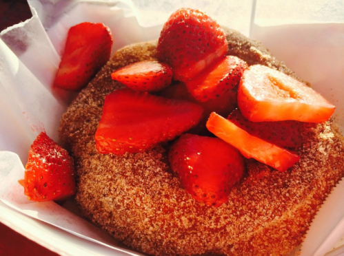 A cinnamon sugar donut topped with fresh, sliced strawberries in a white paper container.
