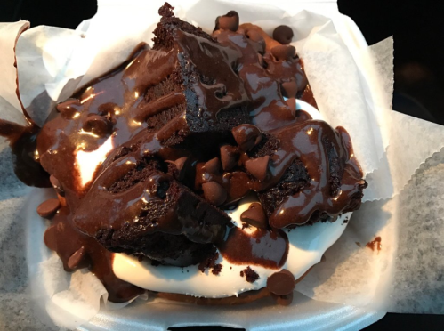 A dessert bowl featuring chunks of chocolate brownie topped with chocolate sauce and chocolate chips on a creamy base.