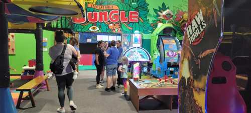 A colorful arcade with kids and adults playing games and enjoying the vibrant jungle-themed decor.