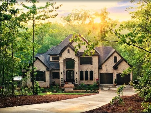 A beautiful brick house surrounded by lush greenery, with sunlight filtering through the trees at sunset.