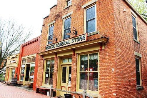 A brick building with a sign reading "Prospect General Store," surrounded by other shops in a quaint town.