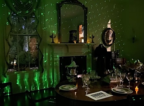 A dimly lit room with green star-like lights, a dining table set with glassware, and a fireplace in the background.