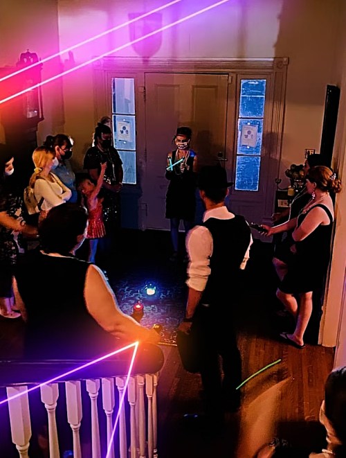 A group of people gathered in a dimly lit room, with colorful lights and a central figure holding a glowing object.