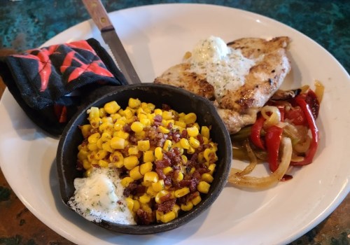 A plate with grilled chicken, sautéed peppers, and a side of corn with butter in a small skillet.