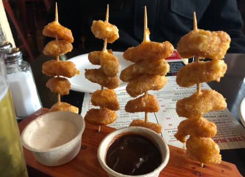 A wooden platter with skewers of crispy fried shrimp and two dipping sauces.