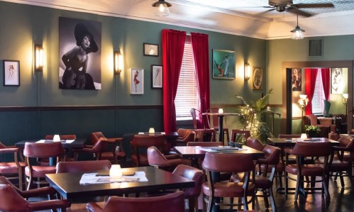 Cozy restaurant interior with red curtains, artwork on the walls, and tables set for dining. Soft lighting creates a warm ambiance.