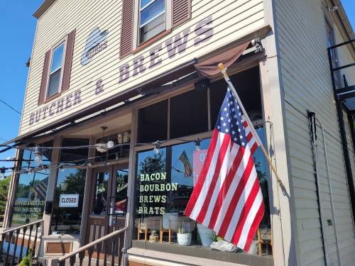 Exterior of a restaurant named "Butcher & Brews," featuring an American flag and a closed sign in the window.